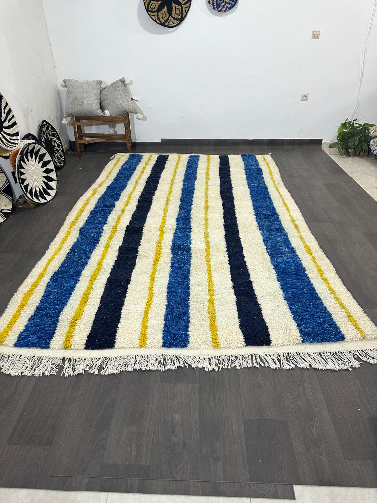 Striped contemporary Moroccan wool rug with blue, yellow, and white colors on a wooden floor.