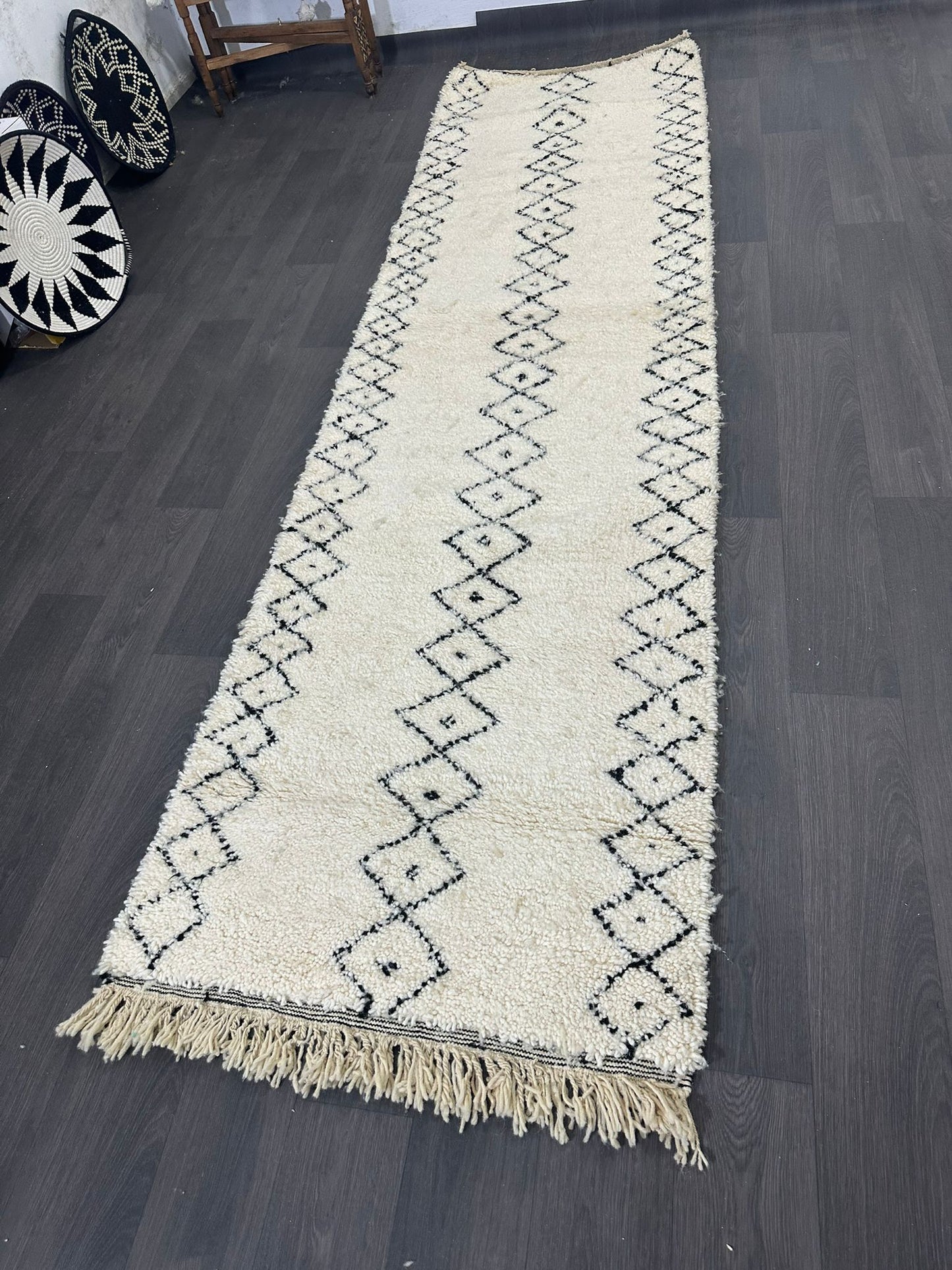 White Moroccan wool rug with black patterns laying on a dark wood floor