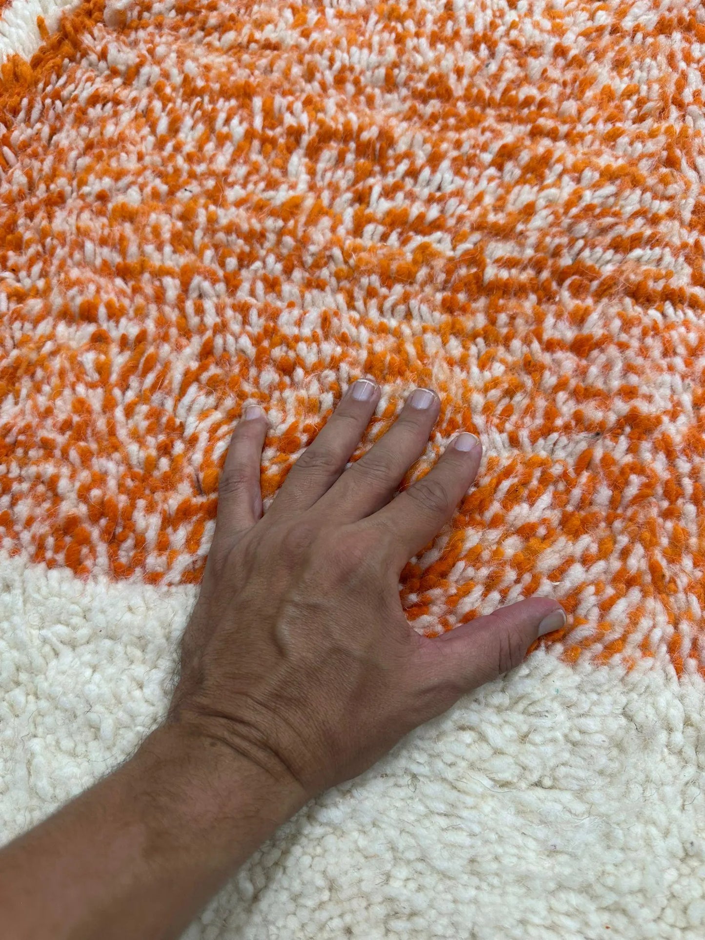 hand touching an orange and off white wool rug