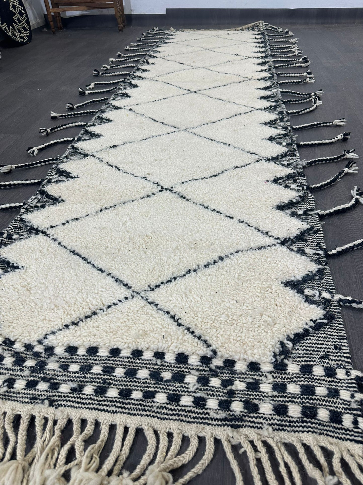Beige and black patterned traditional moroccan rug with tassels on a wooden floor.