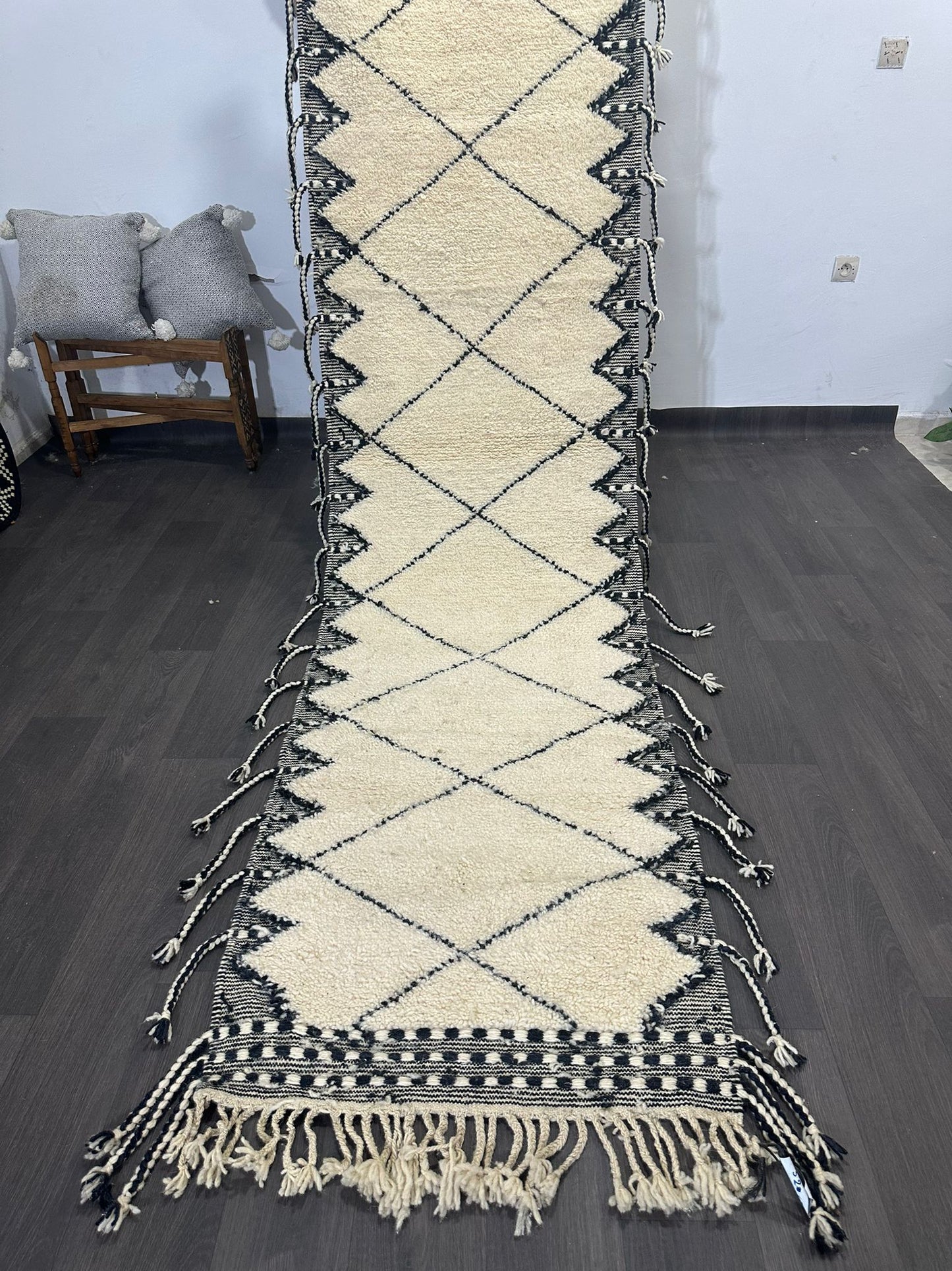 Beige and black patterned traditional moroccan rug with tassels on a wooden floor.