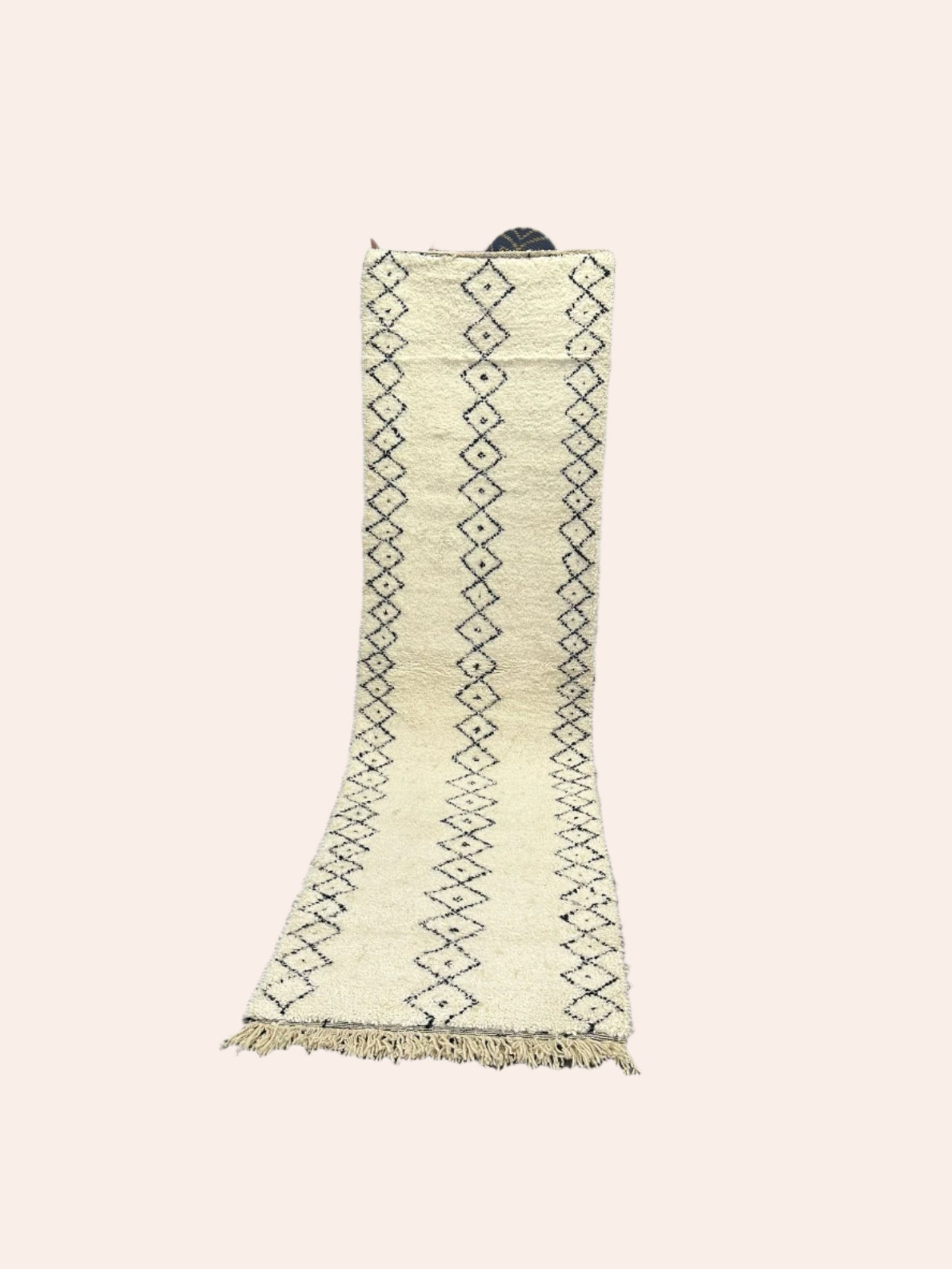 White Moroccan wool rug with black patterns on a wooden floor in a room with white walls.