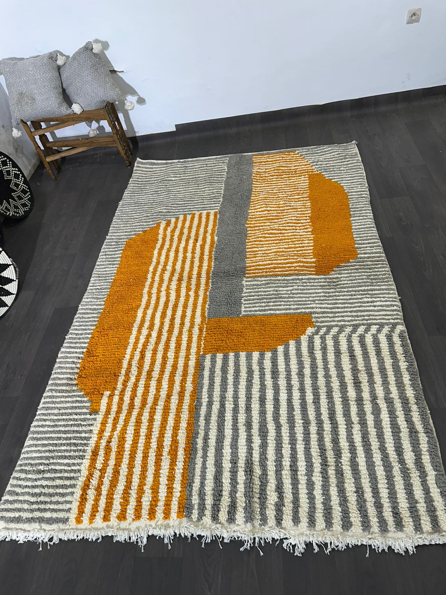 Geometric patterned rug with orange and gray colors on a dark floor.