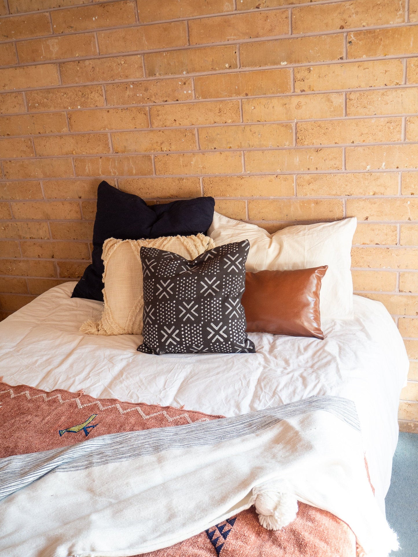 The cushion sitting on the bed with various other cushions behind it from a different angle