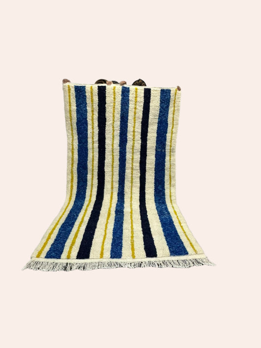 Striped contemporary Moroccan wool rug with blue, yellow, and white colors on a wooden floor.