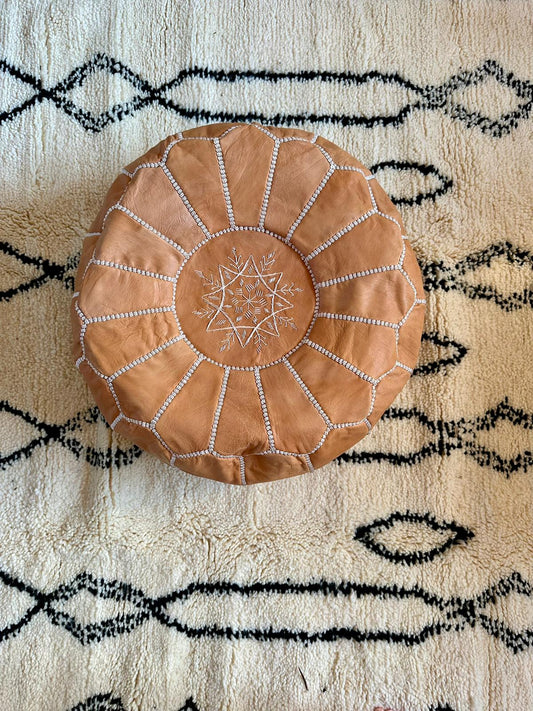 Tan leather ottoman on cream rug with black lines
