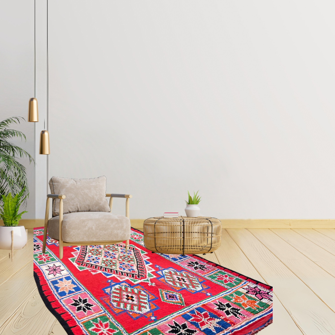 Red Moroccan vintage rug with tribal multi-coloured designs in a room with white walls, single chair, small table and plants