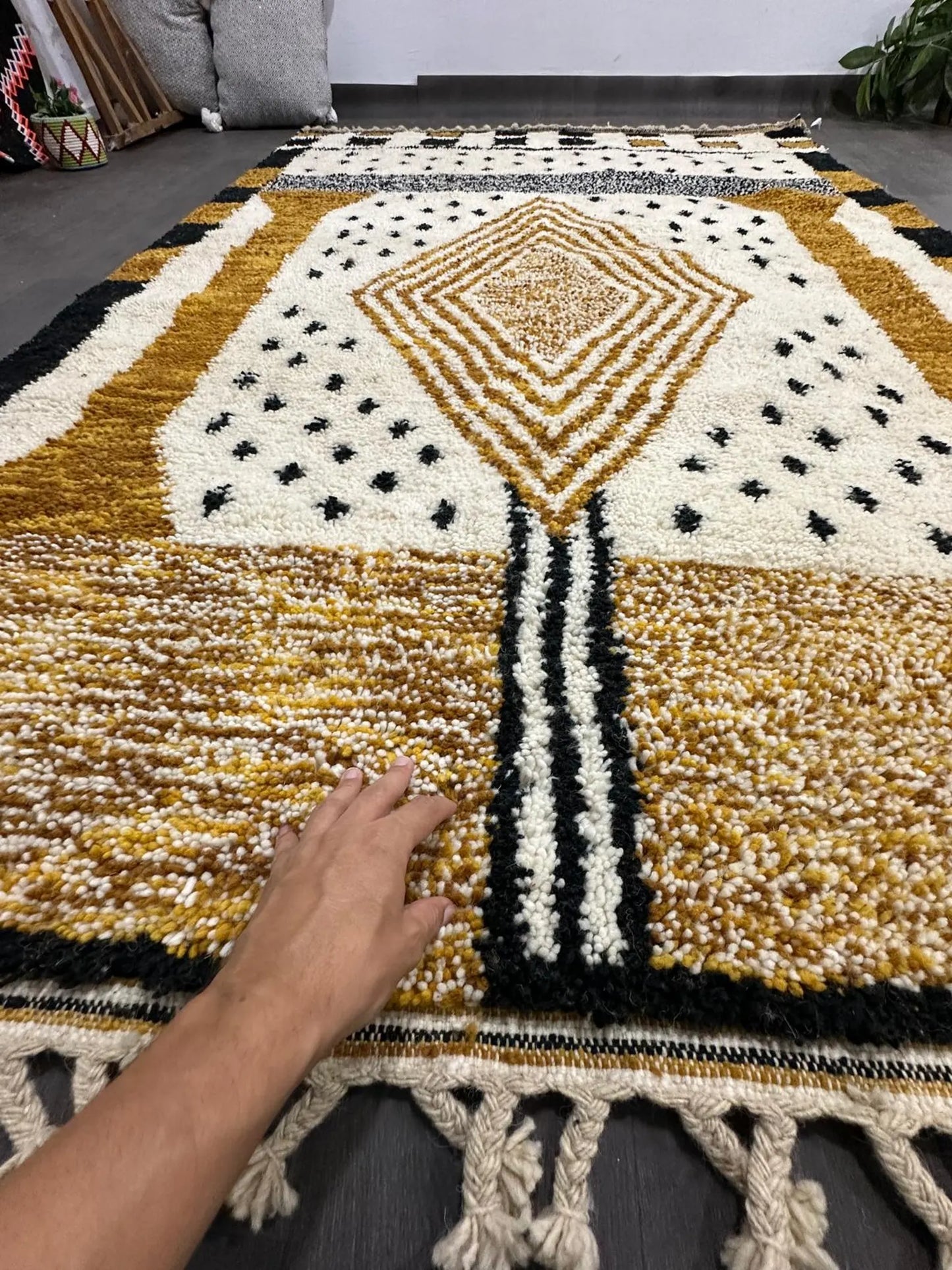 Hand touching a geometric patterned rug with black, gold, and white colors.