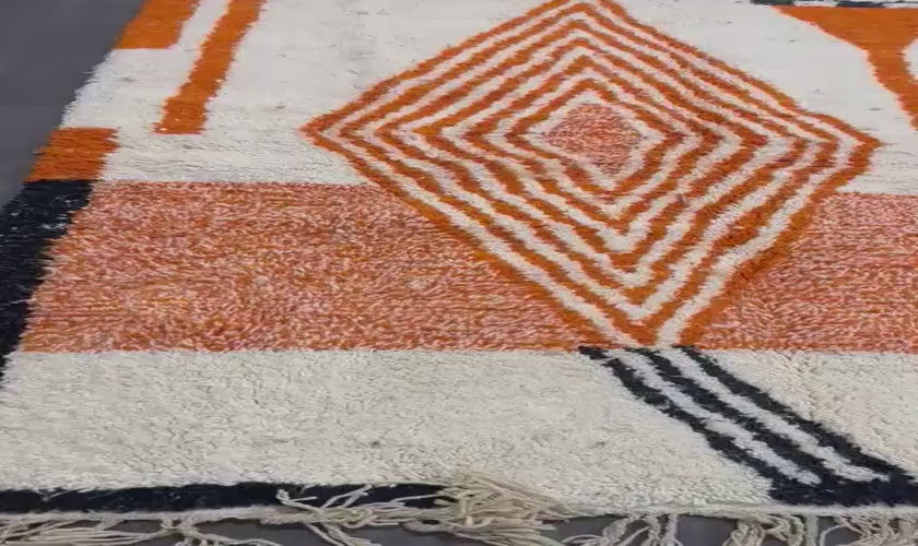 Upclose view of the hana rug. A white wool rug with orange geometric design