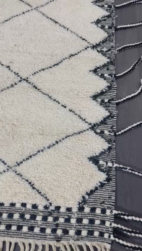 video of Beige and black patterned traditional moroccan rug with tassels on a wooden floor.