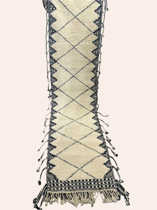 Beige and black diamond patterned traditional Moroccan rug on a dark wooden floor.