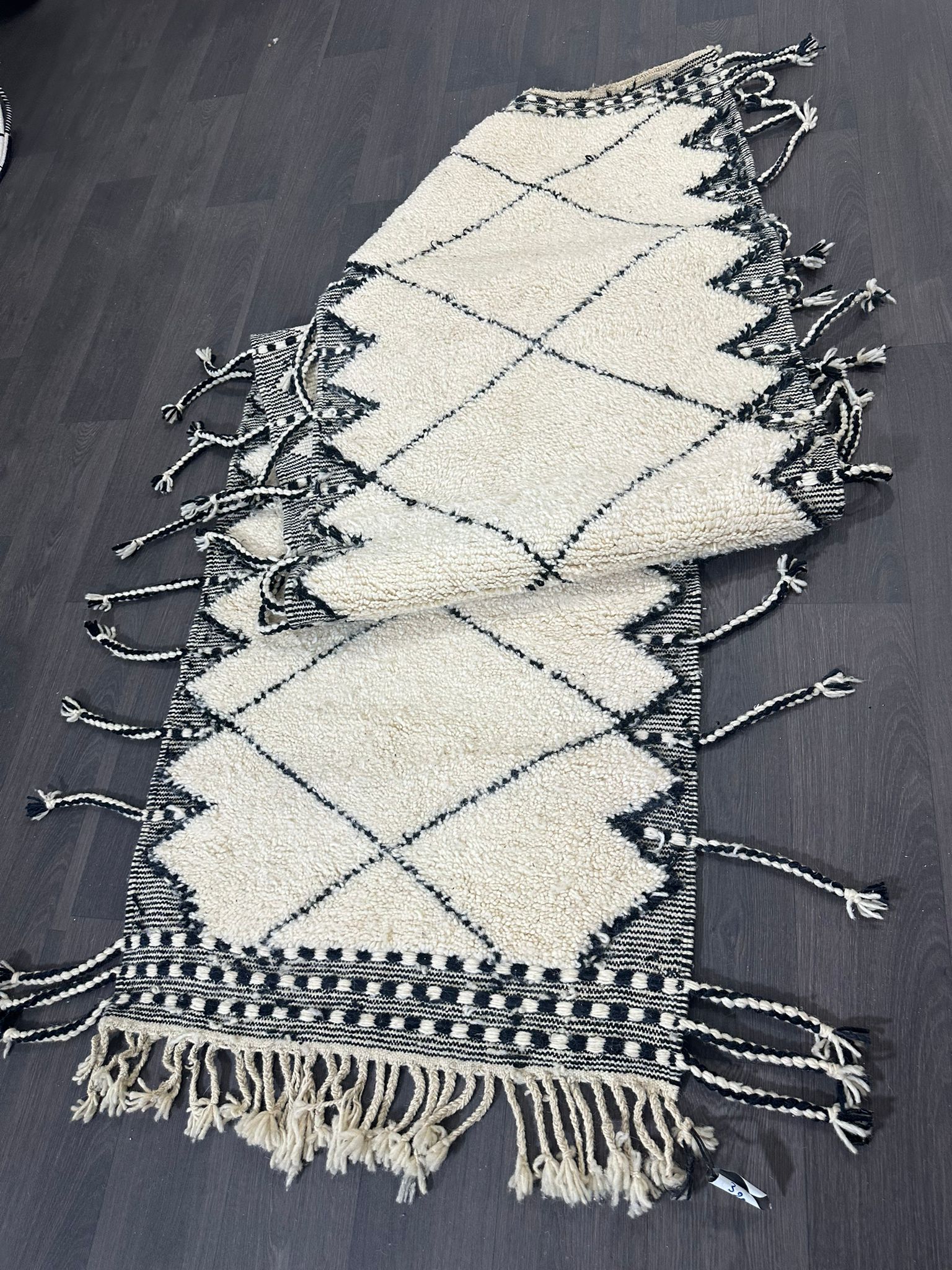 Beige and black patterned traditional moroccan rug with tassels on a wooden floor.