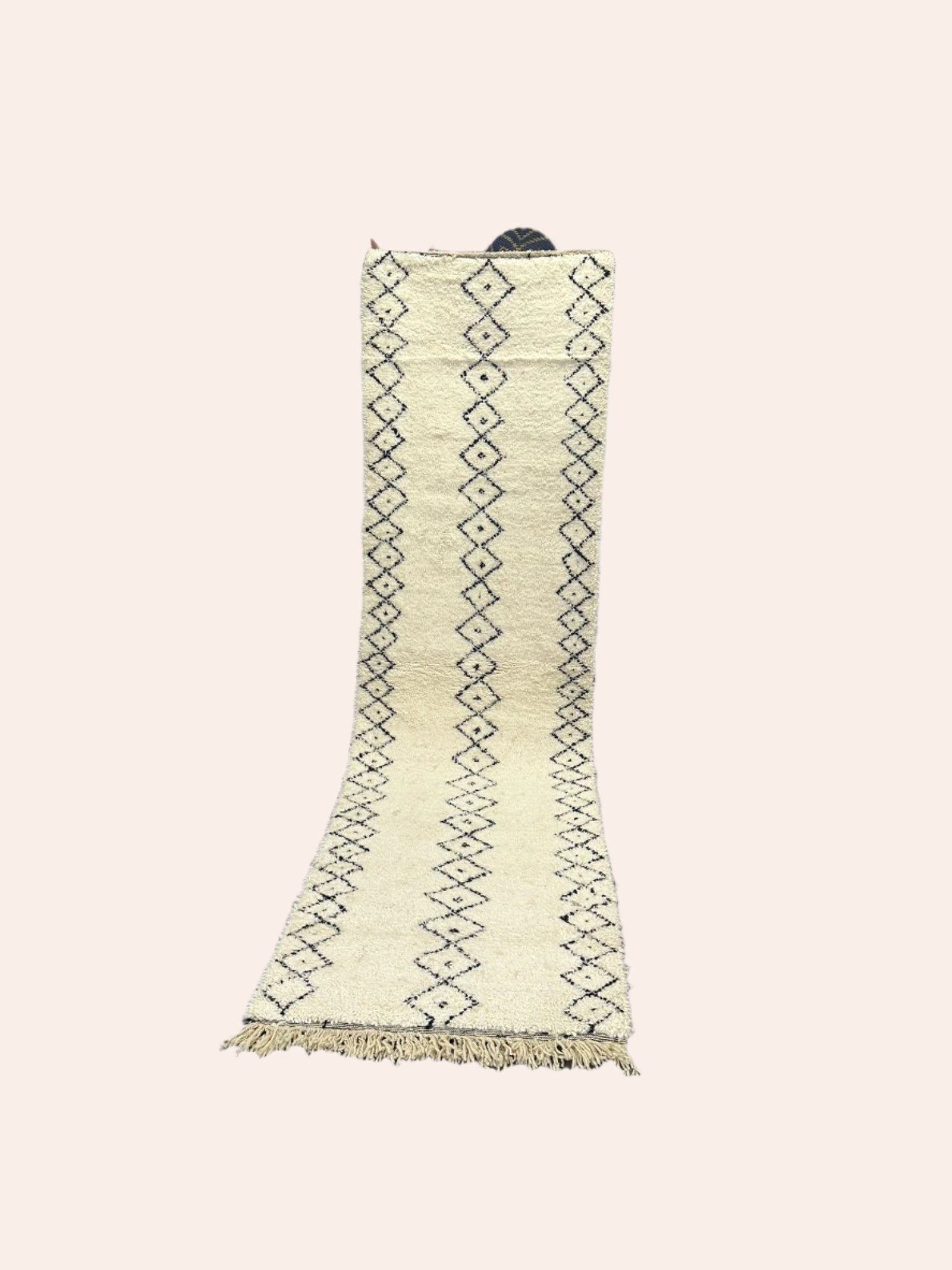 White Moroccan wool rug with black patterns on a wooden floor in a room with white walls.