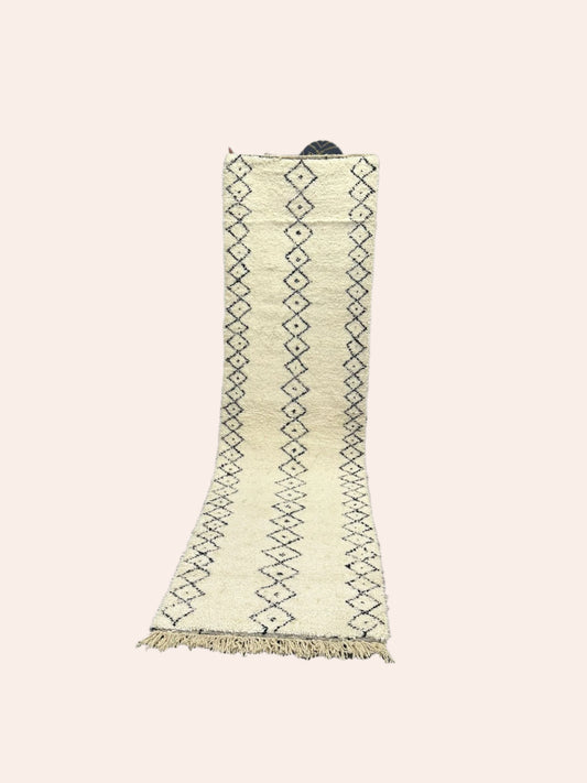 White Moroccan wool rug with black patterns on a wooden floor in a room with white walls.